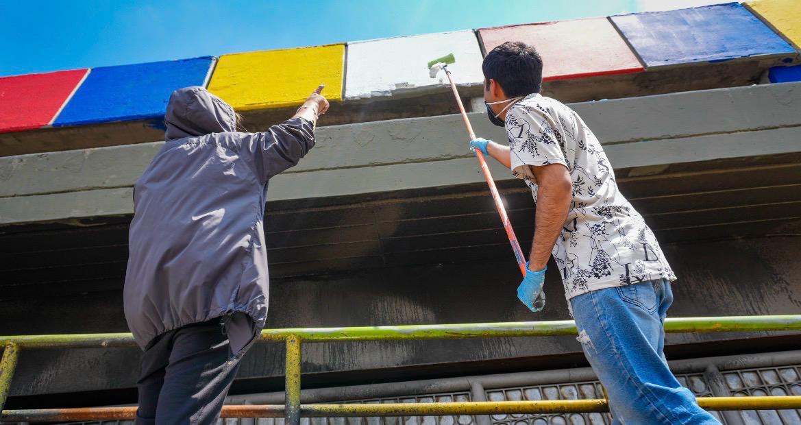 Del comparendo al mural: colados y demás infractores embellecieron puente de la calle 72 con 68 para saldar su deuda con Bogotá Un hombre pintando un puente y otra persona señalándolo